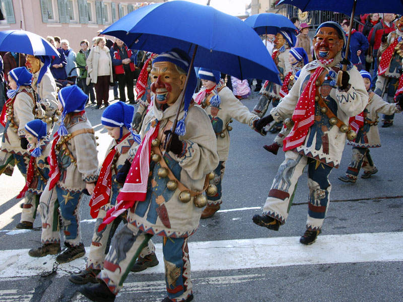 Fasnachtskostüm Bonndorfer Pflumeschlücker mit Glocken, rotem Tuch und blauem Schirm in der Hand.