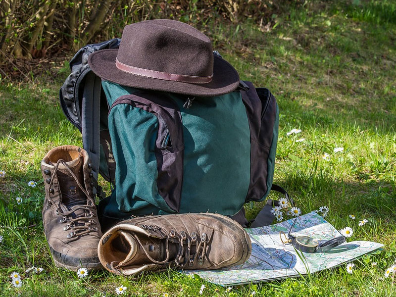 grün-blauer Rucksack mit Wanderschuhen, Landkarte und Kompass auf einer Wiese zum Thema Wanderungen und Sport in Bonndorf.