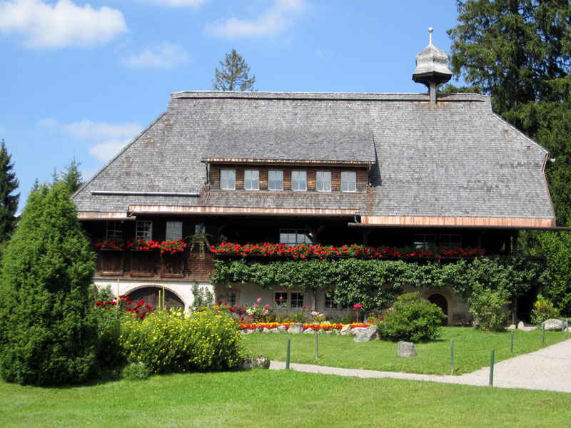 großes Bauerhaus mit Blumen und Grünfläche im Vordergrund. Heimatmuseum Hüsli im Schwarzwald